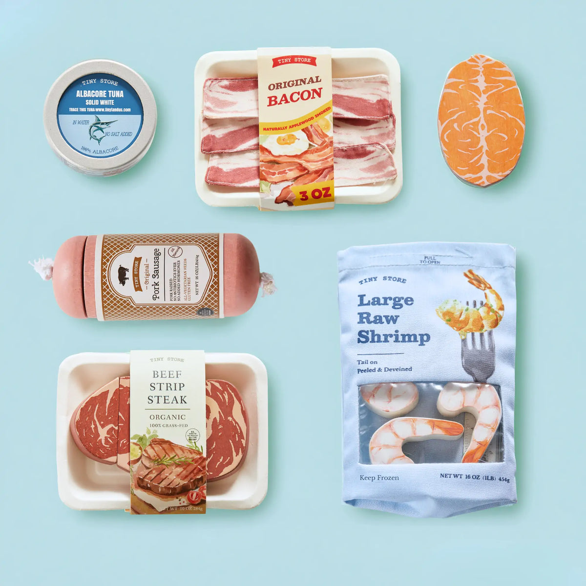 The Tiny Land® Organic Meat & Seafood Pack by Tiny Land Play Food features realistic toy items for toddlers like canned tuna, bacon strips, salmon fillet, sausage, beef strip steak, and raw shrimp on a light blue background.