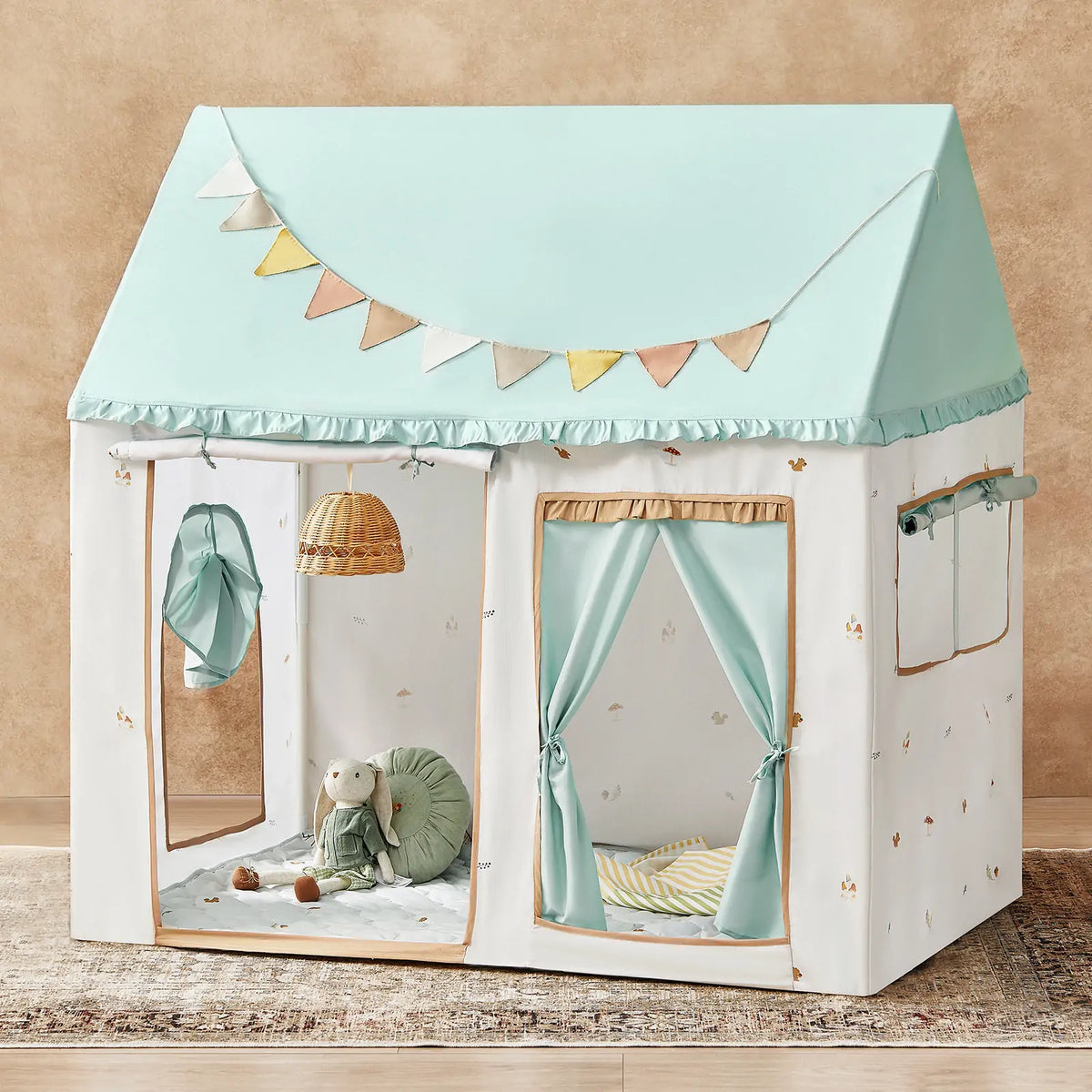 The Tiny Land Nature-inspired Play & Art Set features a Sage Easel and Forest Play House with a mint roof, bunting, windows, curtains, plush toys, cushion, and rattan light for a cozy indoor play space.|green