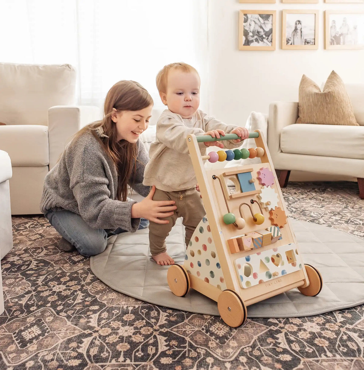 A young child stands holding the Tiny Land® Versatile Natural Wooden Baby Walker as a smiling woman kneels beside them on a patterned rug in a bright, cozy living room|Morandi