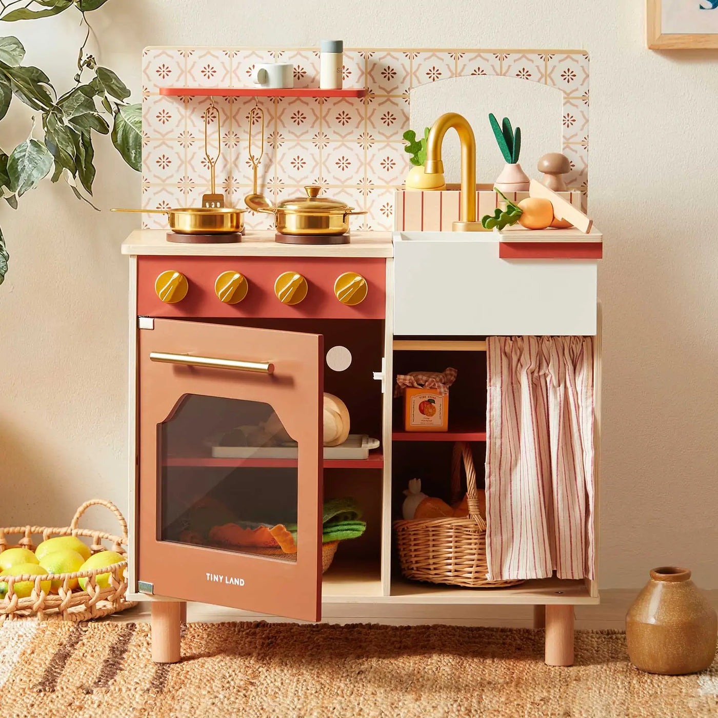 The Tiny Land® Mediterranean Play Kitchen by Tiny Land features a stove, oven, sink, hanging utensils, pots, pans, veggies, and a basket of play food. Pink and gold accents plus patterned tiles add charm to this wooden set|Mediterranean