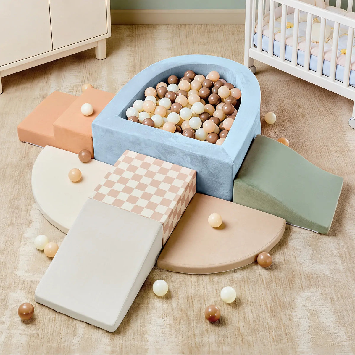 The Tiny Land® PlayNest Climbing Ball Pit Set with Tunnel, featuring soft foam ramps, checker-patterned climbing blocks, a curved ball pit filled with beige, brown, and white balls, sits on a tan carpet near a crib and dresser in an inviting indoor playground nursery.|Blue