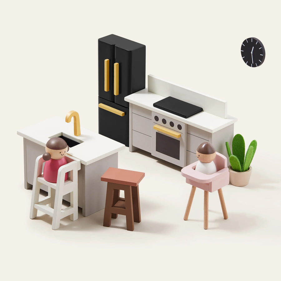 Minimalist clay figures in a modern kitchen scene from the Tiny Land® Sweetwood Edge Dollhouse by Tiny Land, featuring a fridge, stove, sink island with stools, wall clock, potted plant, and two miniature family models seated at the counter.