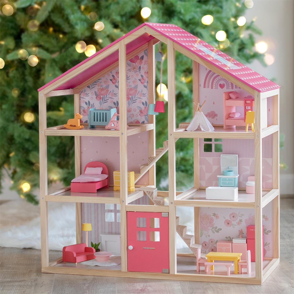A pink dollhouse with furniture set up in front of a Christmas tree.