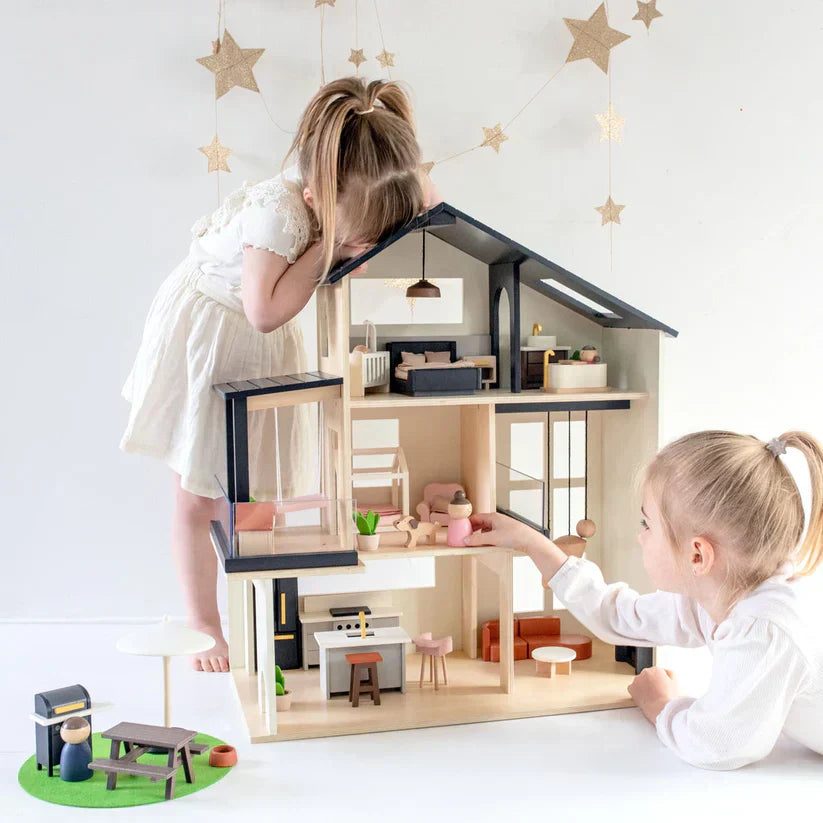 Two young girls in white dresses play with the Tiny Land Sweetwood Edge wooden dollhouse decorated with stars on the wall