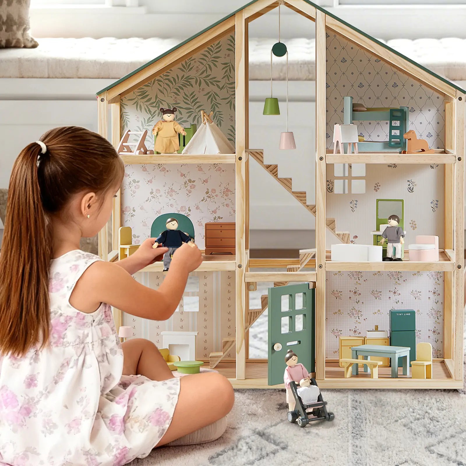 Girl playing with Tiny Land wooden dollhouse, arranging miniature family dolls and furniture for creative pretend play