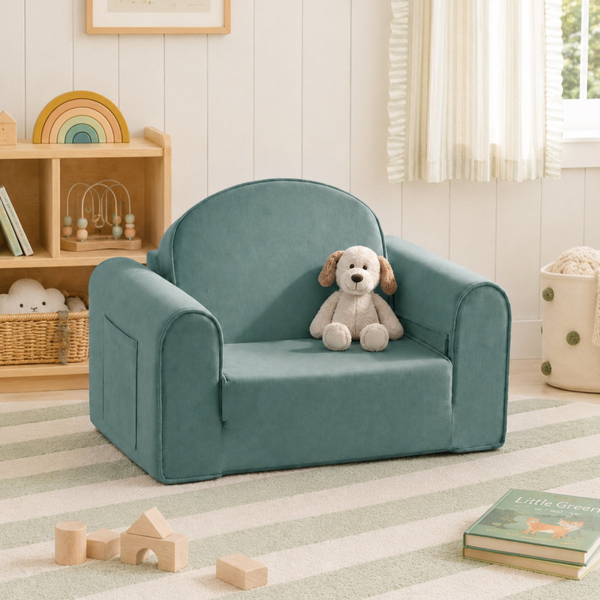 The Tiny Land® GentleSnug Kids Sofa Chair in teal sits with a stuffed dog toy on a striped rug in a cozy, light-filled kids’ room with books, wooden toys, and shelves in the background.