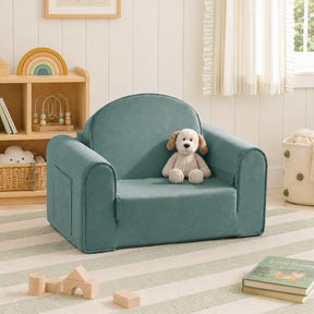 The Tiny Land® GentleSnug Kids Sofa Chair in teal sits with a stuffed dog toy on a striped rug in a cozy, light-filled kids’ room with books, wooden toys, and shelves in the background.