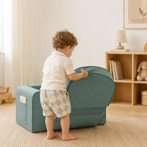 A young child plays with the Tiny Land® GentleSnug Kids Sofa Chair in a cozy, sunlit room furnished with wooden pieces, a bookshelf filled with books and a stuffed bunny, all styled in soft, neutral decor.