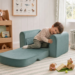 A young boy smiles while relaxing on the Tiny Land® GentleSnug Kids Sofa Chair in a cozy, sunlit room filled with toys, books, and animal-themed decor.