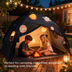 Two children sit inside the Tiny Land® Kids Bed Tent in a backyard at dusk, glowing with string lights and lanterns as they play with a toy campfire. Text: Perfect for camping, campfires, or as an indoor tent for kids to read or play together.|SPACENEST