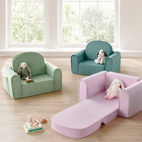 Three Tiny Land® GentleSnug Kids Sofa Chairs—one in green, one in teal, and one in pink—are arranged in a sunlit room. Perfect as playroom furniture from Tiny Land, these cozy seats include a flip-open chair; the pink GentleSnug is unfolded into a sleeper. Stuffed animals sit on each chair, while wooden blocks are scattered across the floor.