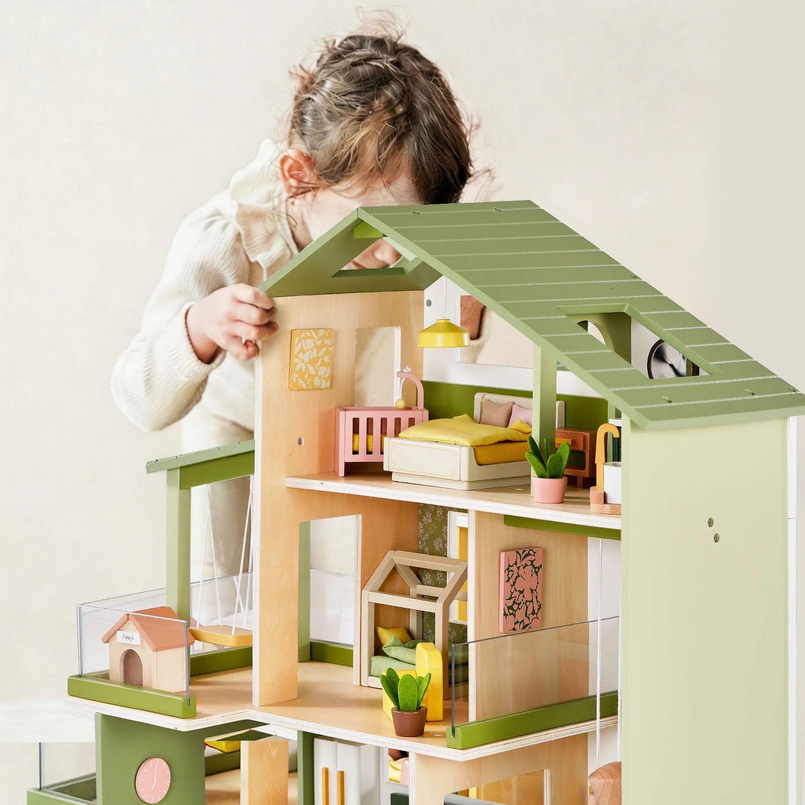 A young child with light brown hair, wearing a cream sweater, arranges miniature furniture and plants inside the detailed rooms of the Tiny Land® Sweetwood Cottage Dollhouse by Tiny Land.|Green