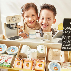 Two smiling children stand behind the Tiny Land® Farm-to-Table Gift Set—a Light & Sound Kitchen & Market Stall by Tiny Land—featuring a toy espresso machine, cash register, and pretend organic foods like yogurt, eggs, and apple juice for endless play.