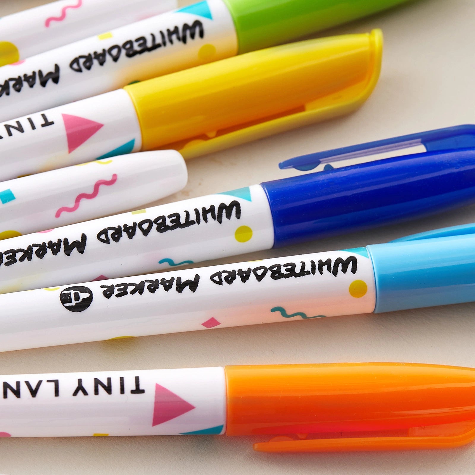Six colorful markers with caps in green, yellow, blue, and orange rest on a white surface. Each marker features playful dots and triangle patterns along the barrel, with "WHITEBOARD MARKER" printed on the side. Designed to complement the Tiny Land® Double-Sided Arched Magnet Chalkboard & Art Kit by Tiny Land, these markers are a creative addition to any child's art supplies or for use on magnetic easels.