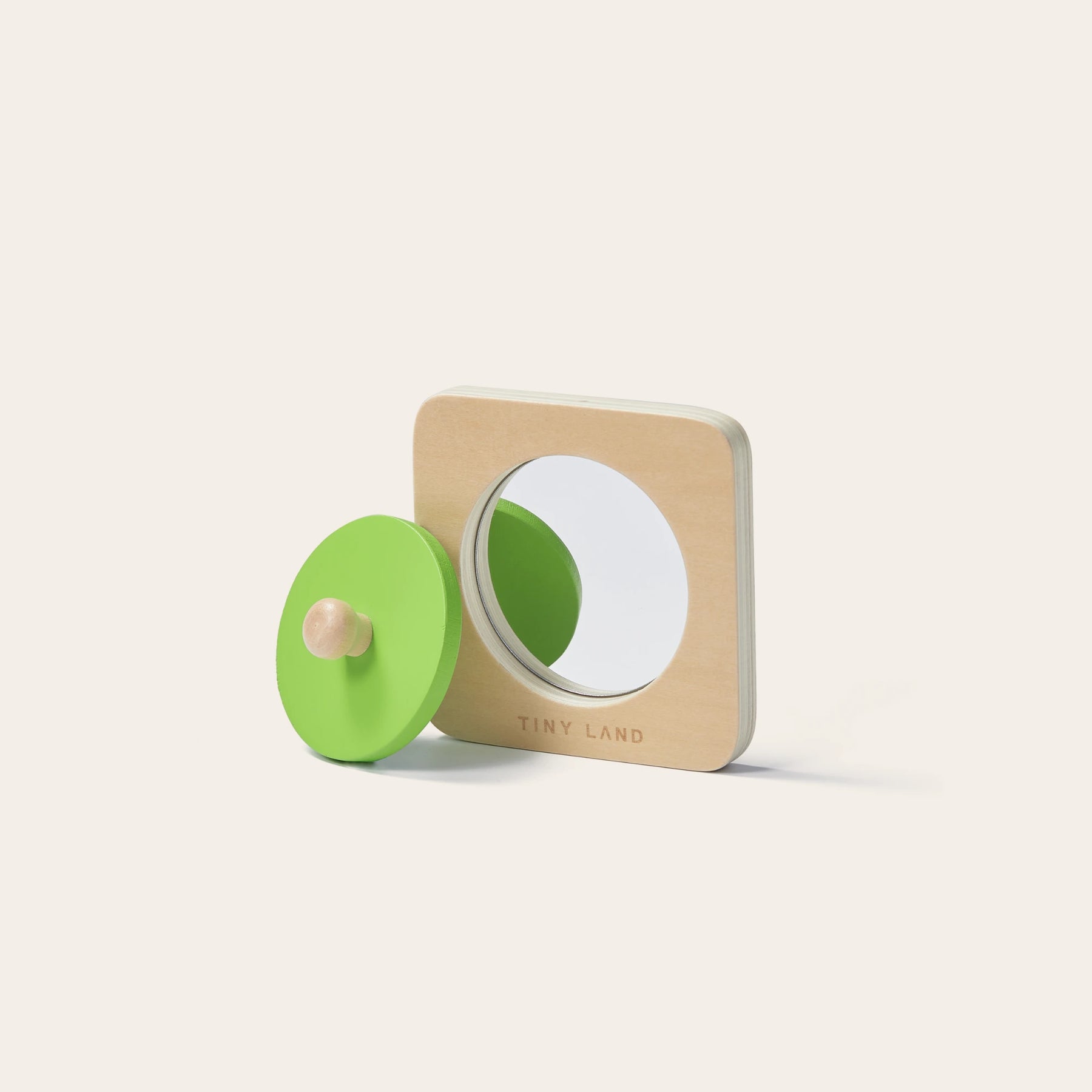 The Tiny Land® Montessori Toys for Newborns (7–9 Months) is a wooden object permanence box with a circular mirror and removable green disc, featuring the engraved Tiny Land brand—ideal for any Montessori toy collection.