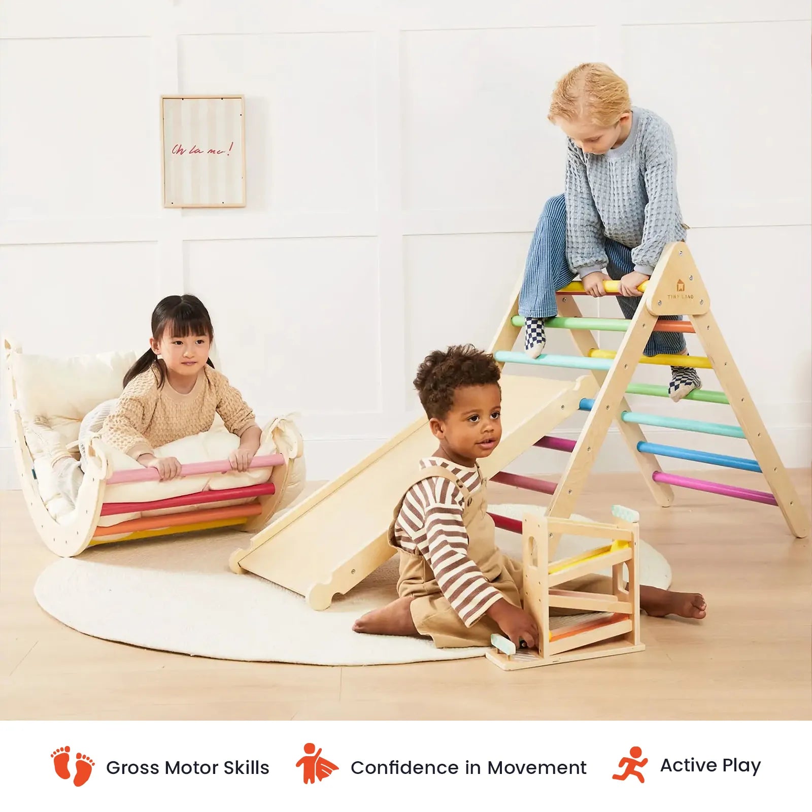 Three children play indoors on vibrant wooden climbing toys, including the Tiny Land® Pikler Triangle 7-in-1 Montessori Climbing Set by Tiny Land; one slides, another sits on the rocker, and a third holds a small climbing frame. The scene encourages gross motor development, confidence, and active play.|rainbow color