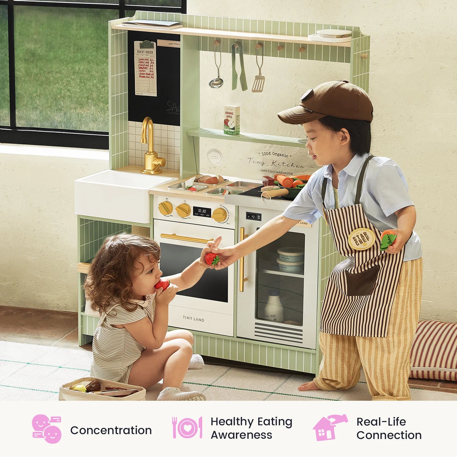 Two young children engage in imaginative play with the Tiny Land® BistroSwitch Play Kitchen. The boy, dressed in a cap and apron, offers a toy tomato to the girl as she enjoys a toy vegetable. Various kitchen toys and utensils from the Tiny Land set are arranged around them. Icons below highlight key developmental benefits of play.|Green