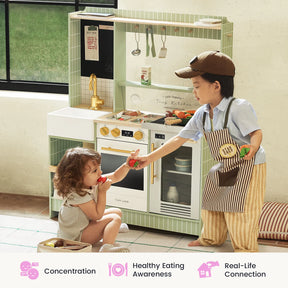 Two young children engage in imaginative play with the Tiny Land® BistroSwitch Play Kitchen. The boy, dressed in a cap and apron, offers a toy tomato to the girl as she enjoys a toy vegetable. Various kitchen toys and utensils from the Tiny Land set are arranged around them. Icons below highlight key developmental benefits of play.|Green