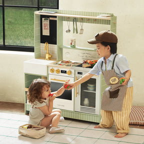 Two kids enjoy pretend play with the Tiny Land® BistroSwitch Play Kitchen. The older child, dressed as a chef, hands a toy vegetable to the younger one, who pretends to eat while sunlight streams through the window.|Green