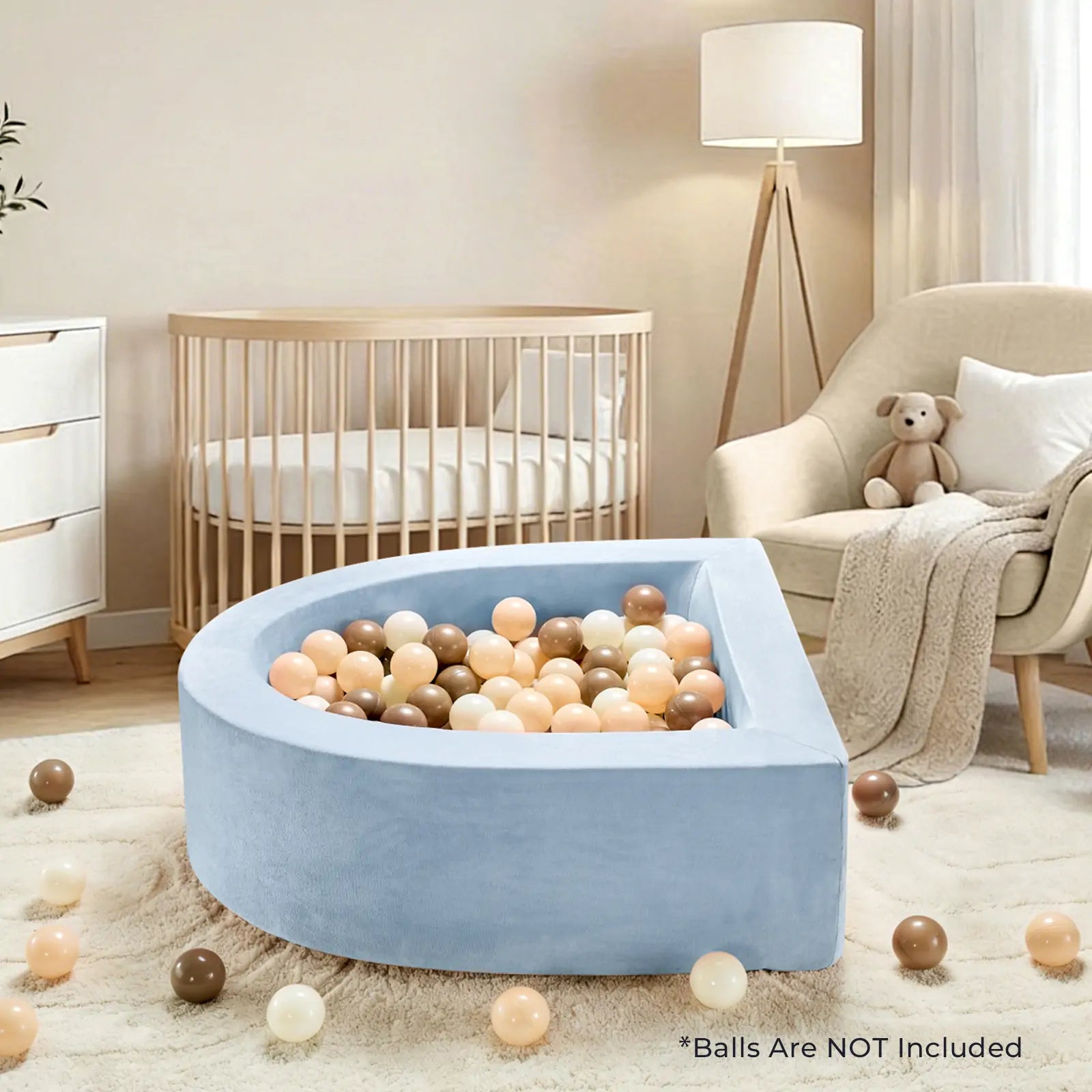 A cozy nursery with a round crib, armchair, teddy bear, lamp, dresser, and a Tiny Land PlayNest Ball Pit (Ocean Balls Not Included) filled with beige, brown, and peach balls. Some balls are scattered on the carpet.|blue