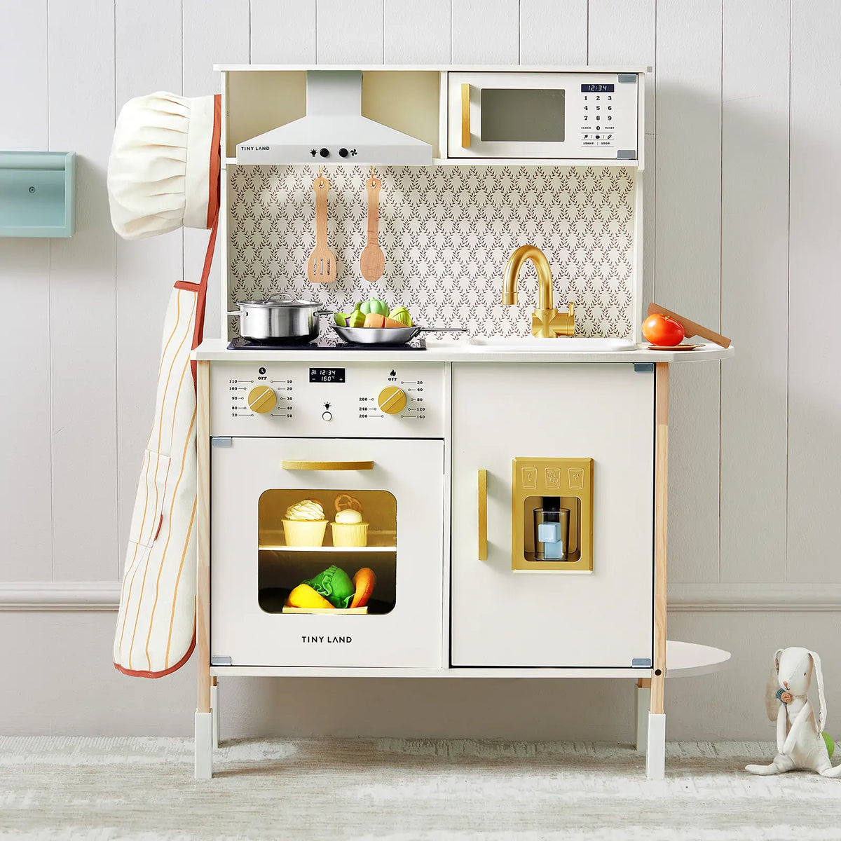 The Tiny Land® PopJoy Kitchen & Fridge Set by Tiny Land is a kids’ pretend playset with chef hat, apron, utensils, toy food, pots, stove, oven, sink, microwave, ice dispenser, plus a stuffed animal and toy carrot for added fun.