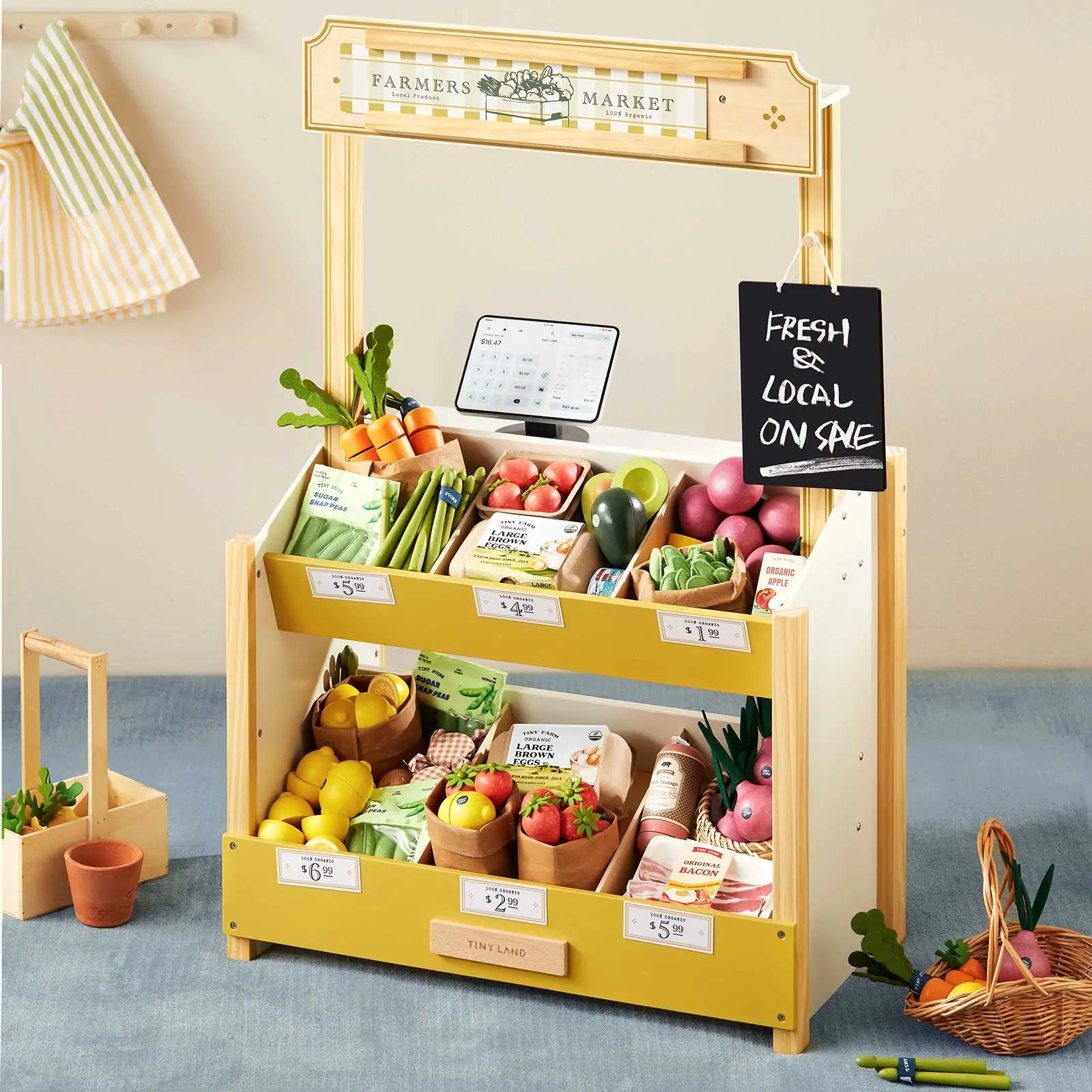 The Tiny Land® Farm-to-Table Gift Set features a wooden market stall with a sign, chalkboard, two shelves with play food and price tags, plus a tote bag and potted plants for endless pretend play. Brand: Tiny Land.