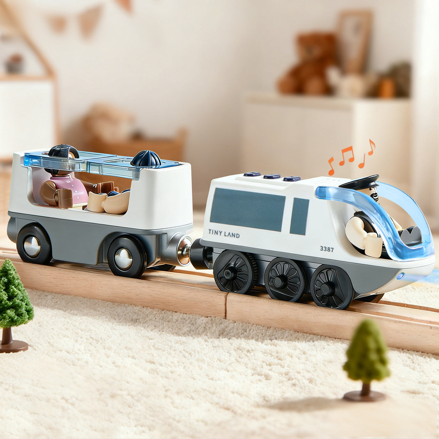 In a cozy playroom, the Tiny Land® Dual-Color Electric Toy Train glides along wooden tracks with two cars carrying animal figurines, trees beside the tracks, and musical notes floating above the front car.|White