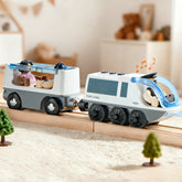 In a cozy playroom, the Tiny Land® Dual-Color Electric Toy Train glides along wooden tracks with two cars carrying animal figurines, trees beside the tracks, and musical notes floating above the front car.|White