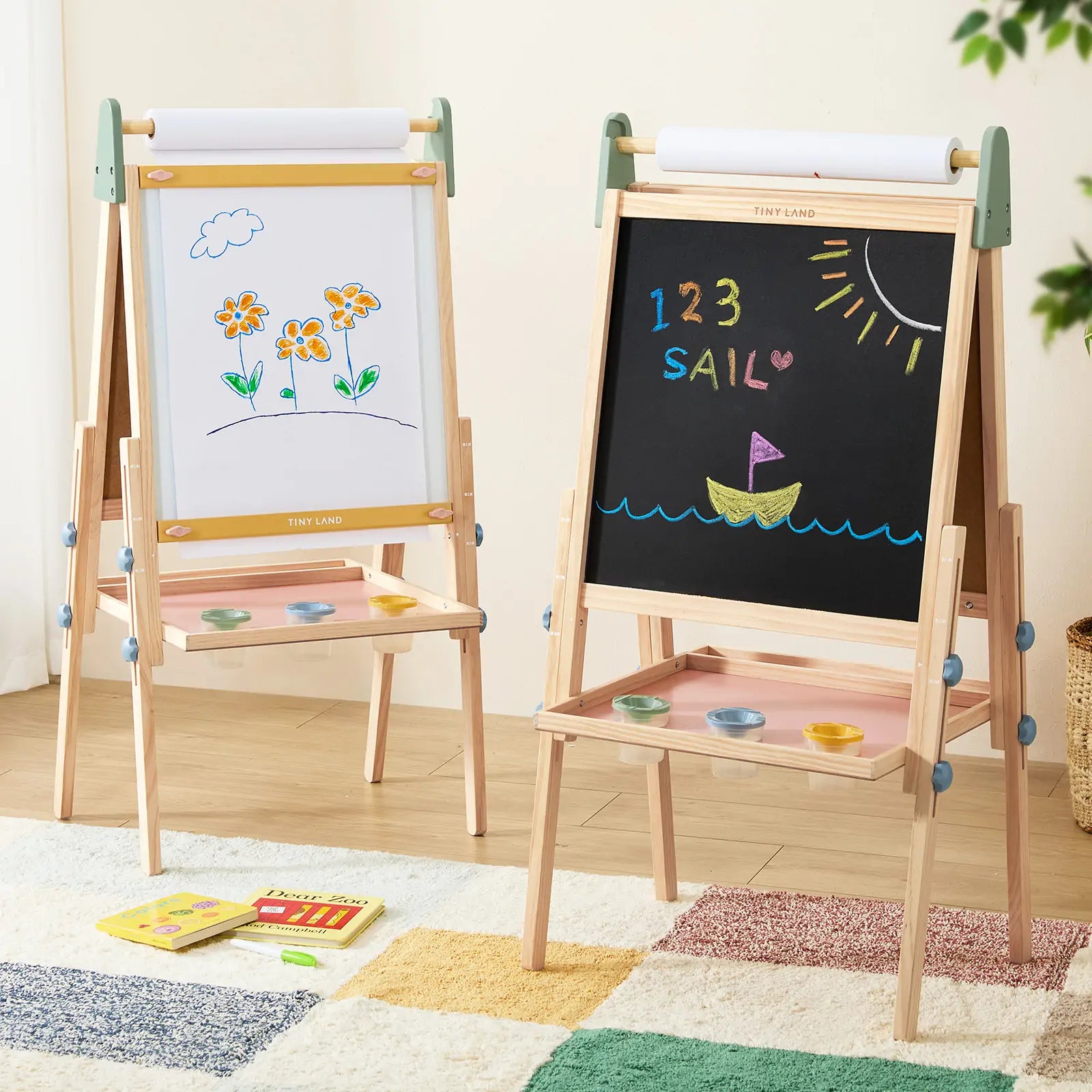 Two Tiny Land® 3-in-1 Art Easels for Kids - Morandi stand on a colorful rug. One shows flower art on paper, the other displays “123 SAIL” and a boat under the sun in chalk. Paint trays are attached below each drawing surface.|green