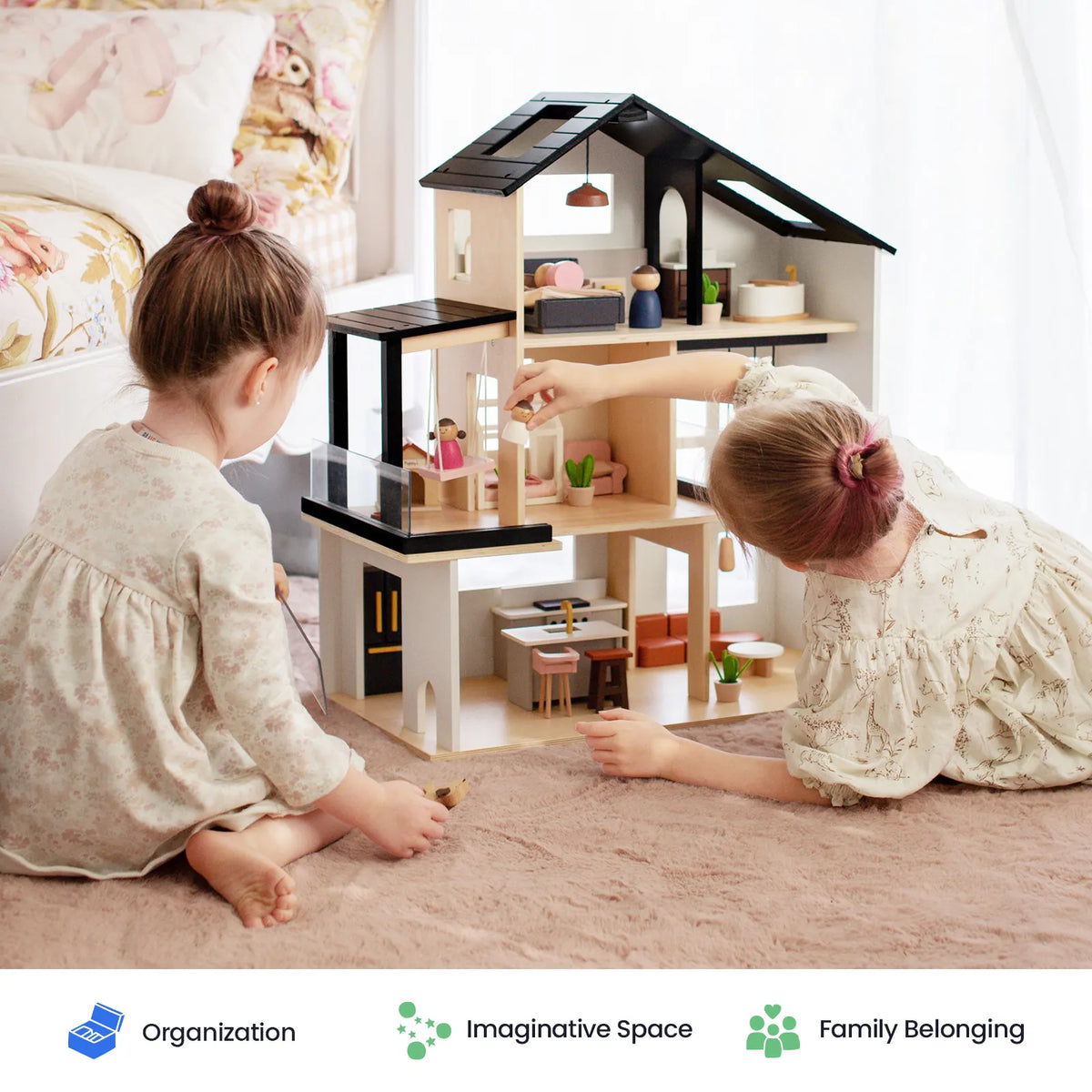 Two young girls sit on a rug, playing with the contemporary Tiny Land® Sweetwood Edge Dollhouse. This detailed dollhouse from Tiny Land features furnished interiors. Three icons below highlight its organization, imaginative space, and sense of family belonging.