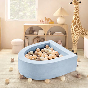 A cozy children's playroom featuring the Tiny Land® PlayNest Ball Pit with 200 Ocean Balls, a large stuffed giraffe, light wooden shelves for toys and books, all bathed in soft natural light from the window.