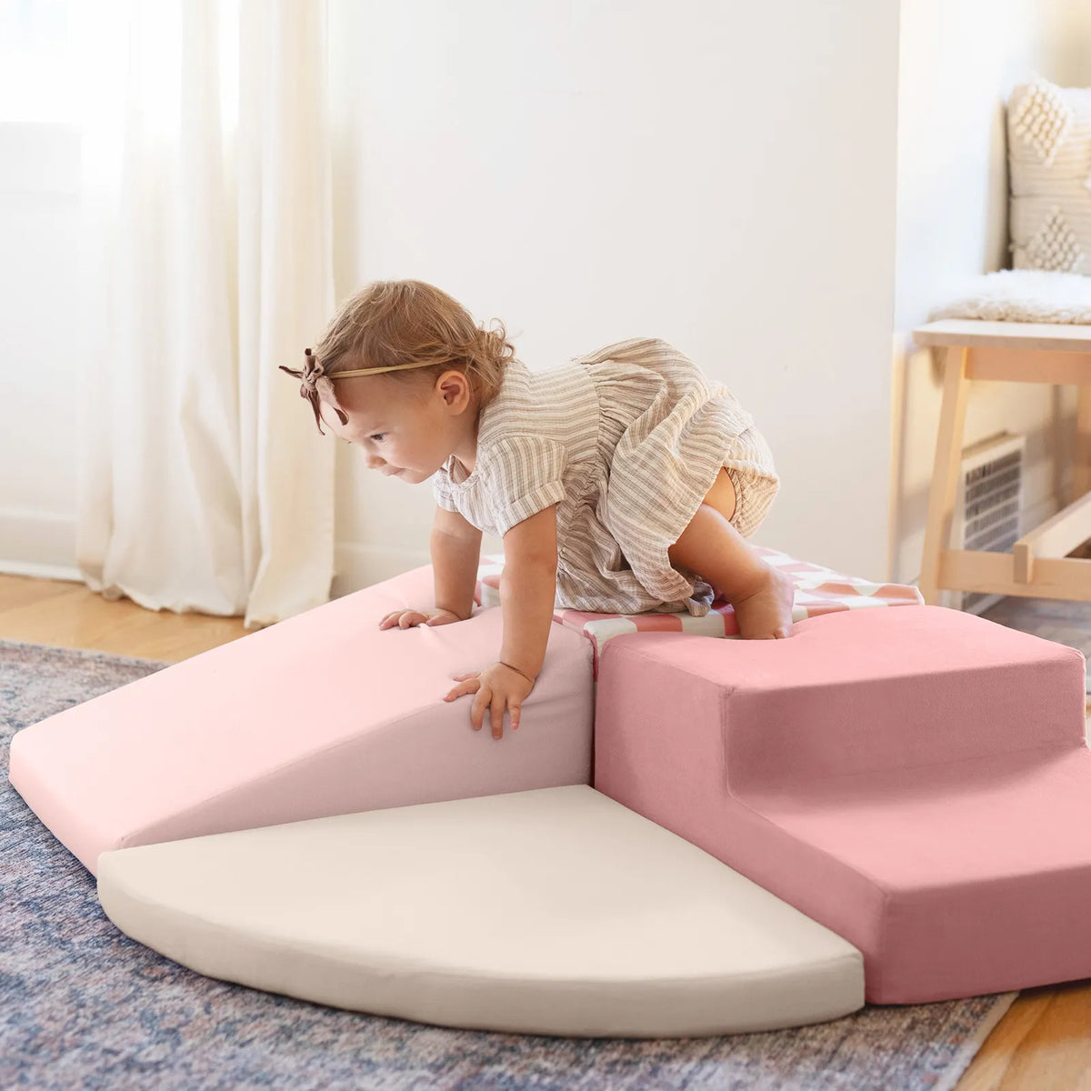 A toddler in a striped dress climbs on the soft, pink and white Tiny Land® Violet PlayNest Climbing Ball Pit Set with Tunnel in a sunlit room featuring a rug, chair, curtained window, and an inviting indoor playground.|Blue