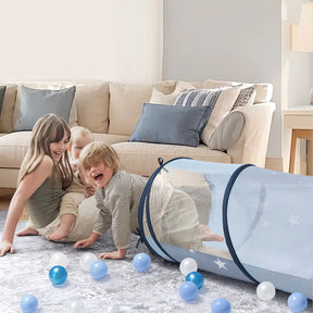 Two young children play on a living room rug with the Tiny Land® Adventure Play Tunnel - Blue by Tiny Land and scattered blue and white plastic balls, while a beige couch with blue pillows sits in the background.|blue