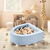 A children’s room features the Tiny Land® PlayNest Soft Foam Ball Pit by Tiny Land—an inviting, blue teardrop-shaped pit (balls not included) ideal for sensory play. The scene includes a large plush giraffe, light wood shelves, and pastel balls filling the ball pit and scattered on the carpet. Text on image: Balls are NOT included.