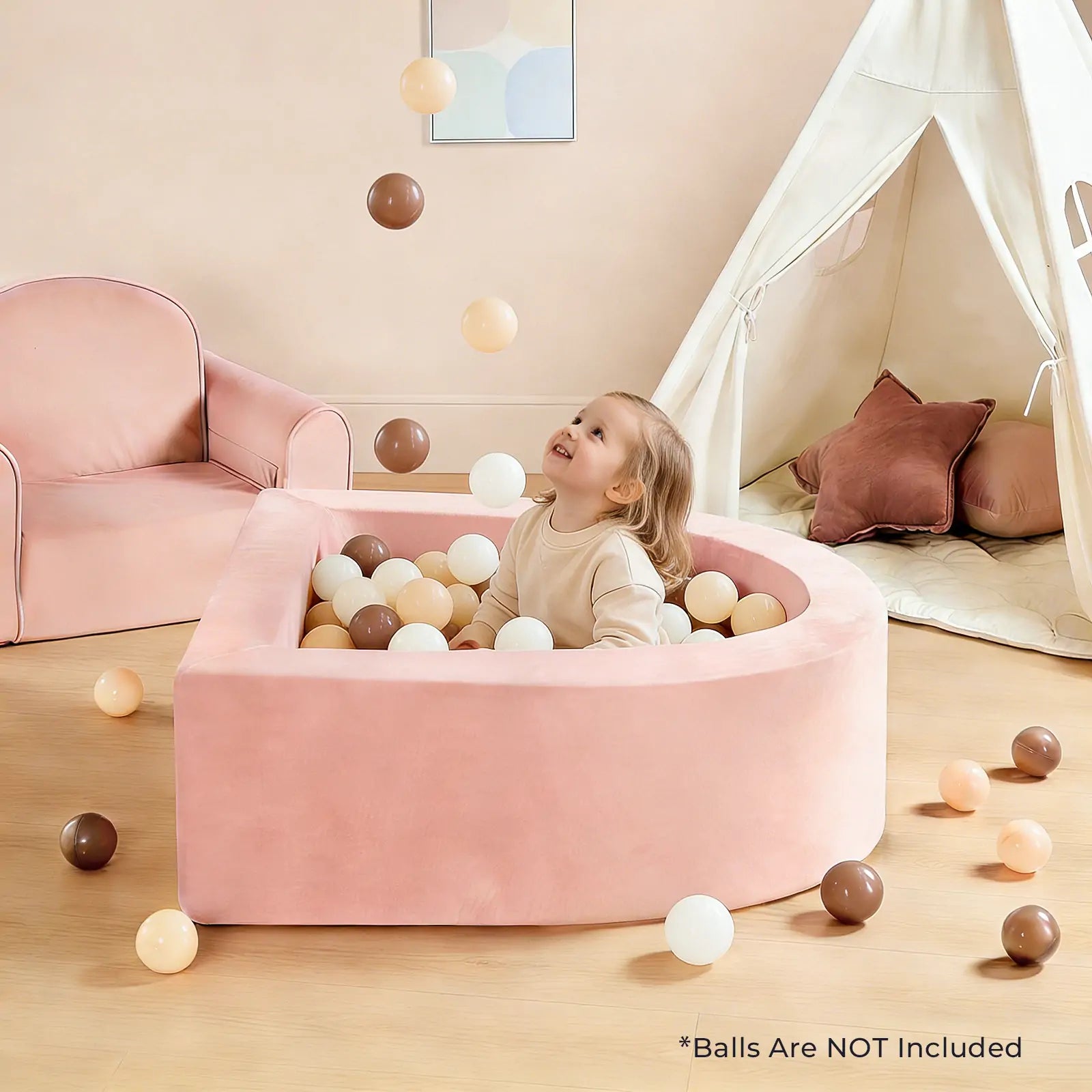 A young child sits happily in the Tiny Land® PlayNest Ball Pit – Ocean Balls Not Included, surrounded by beige, white, and brown balls. The child laughs as balls float nearby; a pink chair and white play tent are visible in the background.|pink