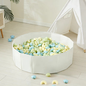 A white playpen filled with Tiny Land® Fun-Shapes Ocean Ball - 200 pcs in pastel green, yellow, and blue and star-shaped toys sits on a light wooden floor near a white teepee tent and a plant. Some Tiny Land balls are scattered outside.|Fun-Shapes
