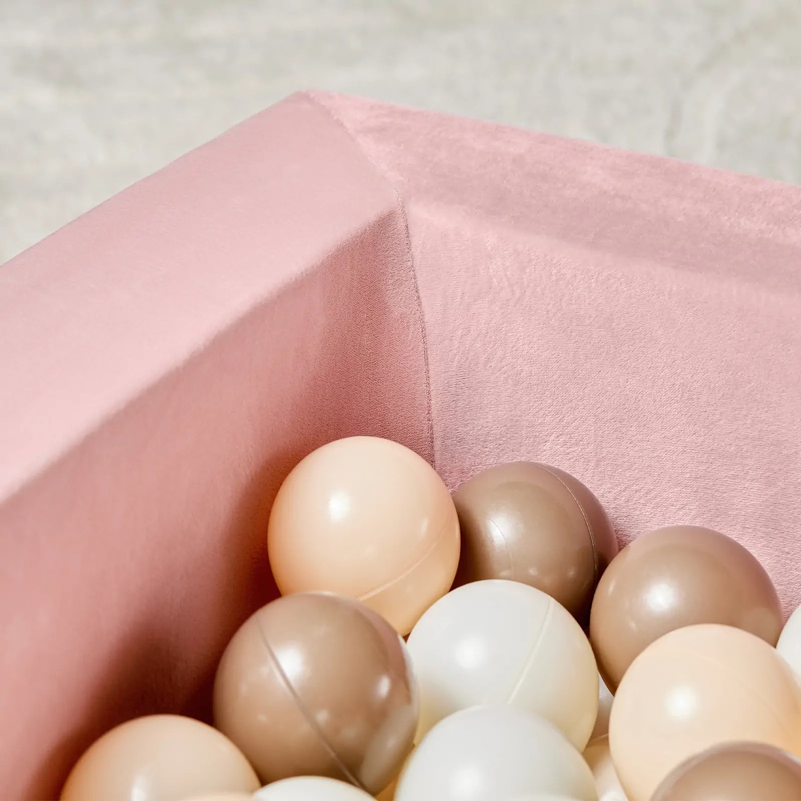 A close-up of the Tiny Land® PlayNest Ball Pit by Tiny Land, velvet-lined in pink and filled with 200 pastel ocean balls in cream, beige, and brown—perfect for creating a cozy toddler play space against a soft, neutral backdrop.