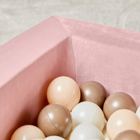 A close-up of the Tiny Land® PlayNest Ball Pit by Tiny Land, velvet-lined in pink and filled with 200 pastel ocean balls in cream, beige, and brown—perfect for creating a cozy toddler play space against a soft, neutral backdrop.
