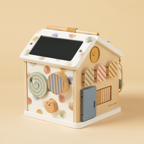 The Tiny Land Cozy Learning Playset includes a wooden Montessori activity cube and playmat, featuring colorful shapes, polka dots, a blue door, chalkboard roof, spinning discs, and smiling faces on a light beige background.