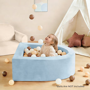 A young child smiles while sitting in a Tiny Land® PlayNest Ball Pit - Ocean Ball Not Included, filled with brown and beige balls, some tossed in the air. In the background are a sofa, decorative pillows, and a play tent.|blue