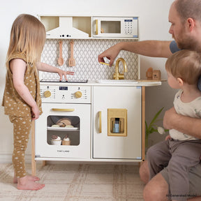 A young girl and an adult with a toddler enjoy imaginative pretend play with the Tiny Land® PopJoy Play Kitchen by Tiny Land, which features utensils, an oven, and a sink—perfect for cooking and washing dishes together.