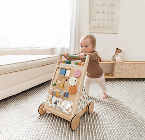 In a cozy, sunlit room with soft carpeting and toys, a baby pushes the Tiny Land Complete Development Playset — Baby Walker + Activity Cube, an ideal choice for encouraging curiosity and developing fine motor skills.
