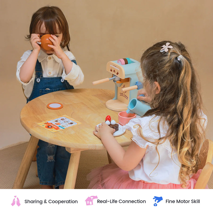 Two young children play at a small round table with the Tiny Land® Play Kitchen Accessories – Children’s Coffee Maker, a wooden kids play coffee maker set. One sips from a cup while the other embraces the barista role, pretending to pour coffee with the Tiny Land wooden coffee maker. Icons below highlight sharing, real-life connection, and fine motor skills.