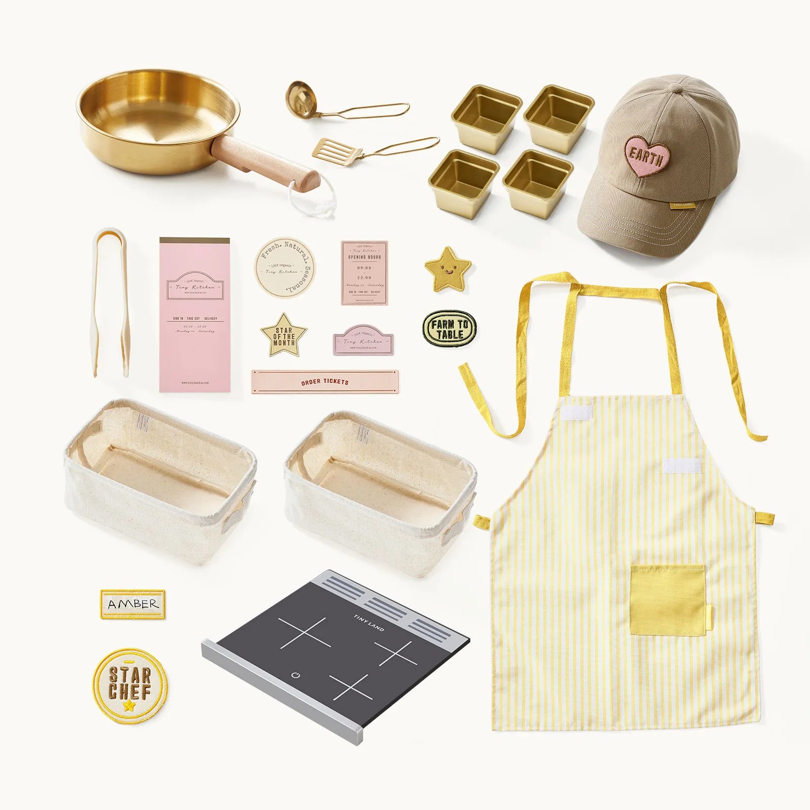 The Tiny Land® BistroSwitch Play Kitchen includes a gold pan, utensils, gold baking molds, apron, cap with Earth patch, recipe cards, kitchen badges, oven dishes, and a black induction cooktop—ideal for pretend play.|White