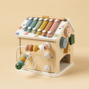 The Tiny Land Cozy Learning Playset combines a playmat with a wooden house-shaped Montessori activity cube featuring a colorful xylophone roof, bead maze, spinning face blocks, and pastel colors on a light beige background.