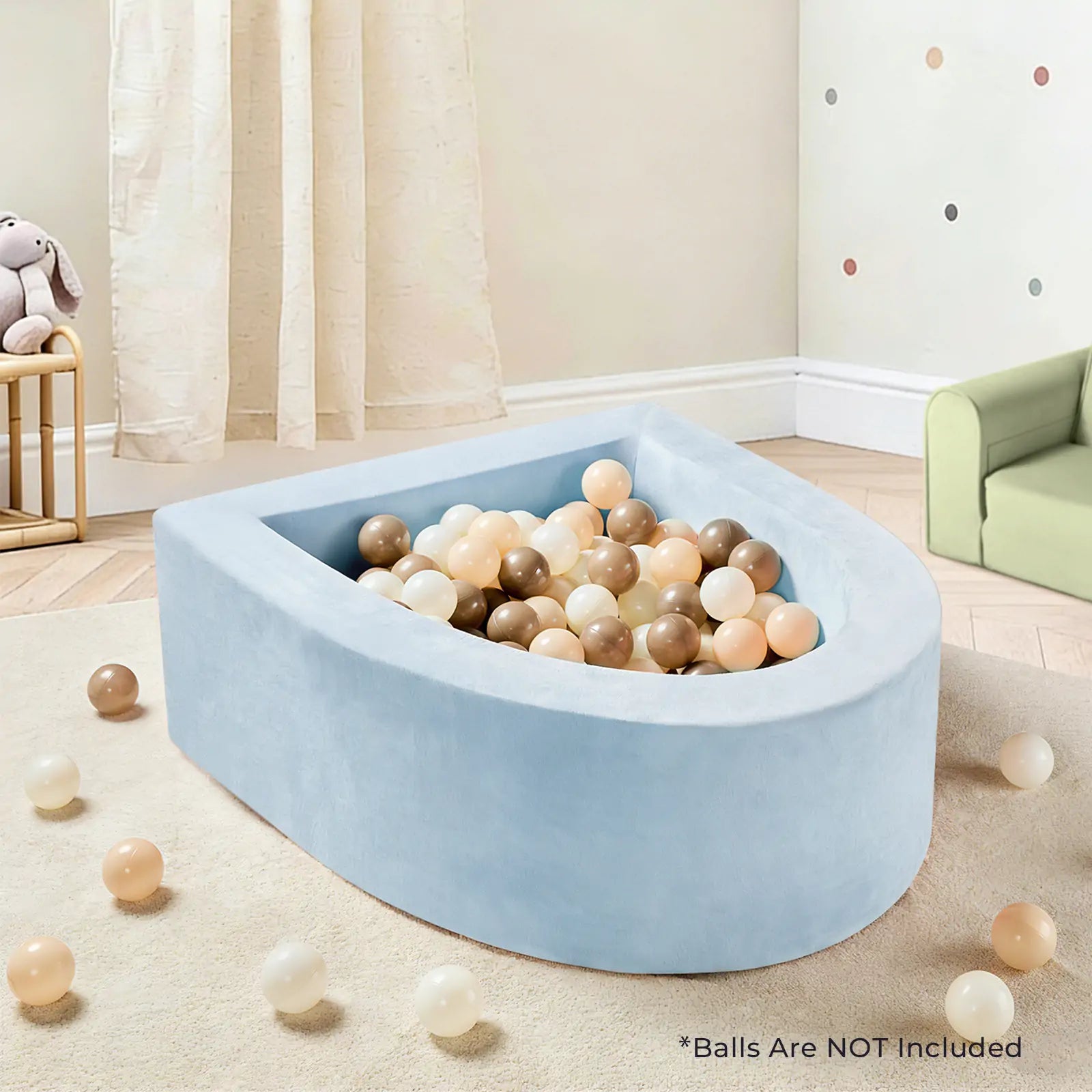 A Tiny Land® PlayNest Ball Pit - Ocean Ball Not Included in light blue sits in a kids' playroom with beige, brown, and cream balls scattered around, a green couch, and a stuffed toy on a chair. Text notes: "Balls Are NOT Included.|blue