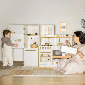 A woman and child enjoy the Tiny Land® Play Kitchen Accessories – Wooden Cabinet Refrigerator for Kids. The woman kneels, smiling with a tray, as the child stands nearby in a bright room with minimal decor and a rug.