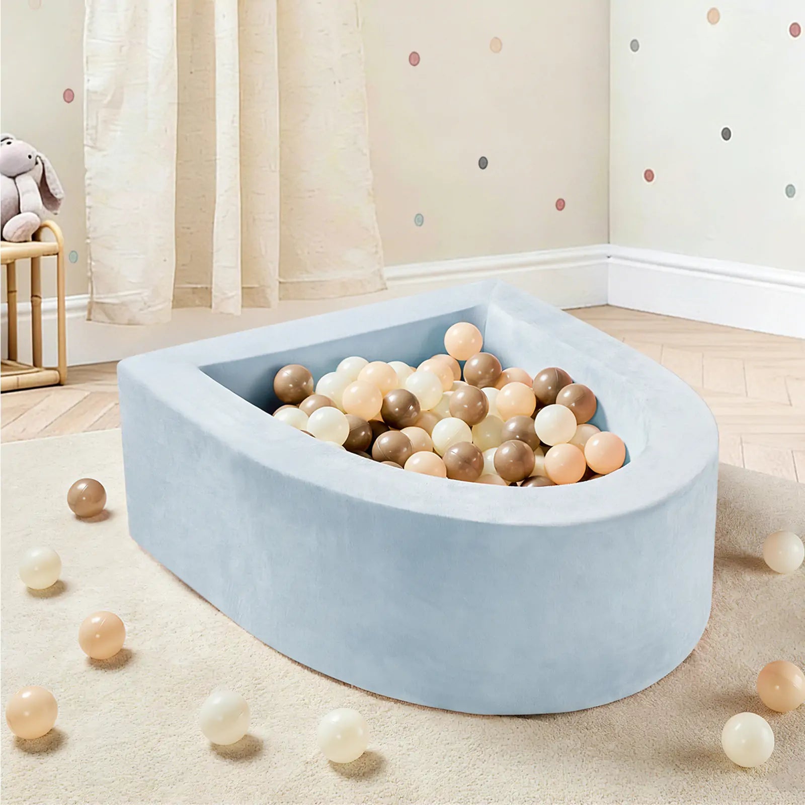 The Tiny Land® PlayNest Ball Pit with 200 Ocean Balls by Tiny Land, in light blue semi-circular design, is featured in a child's room with wooden floors, a curtain, polka-dot wall decor, and a stuffed rabbit on a stool.