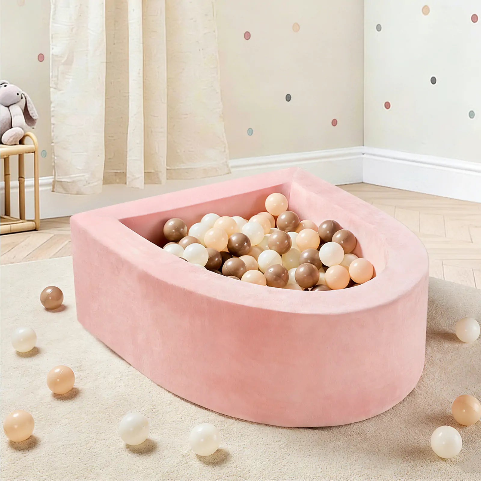 The Tiny Land® PlayNest Ball Pit with 200 Ocean Balls by Tiny Land, in pink and boat-shaped, is featured in a toddler play space with wooden floors and dotted wallpaper. A toy rabbit sits on a shelf in the background.