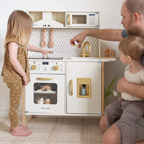 A young girl and an adult man with a toddler enjoy pretend play in the Tiny Land® Farm-to-Table Play Set, featuring an interactive kitchen, storage fridge, and organic food collection—all by Tiny Land.